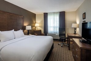 A hotel room with a large bed, a desk with a TV, a chair, a lamp, and a window with curtains.