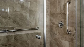 Ducha con puerta de cristal, paredes de mármol y barandilla.