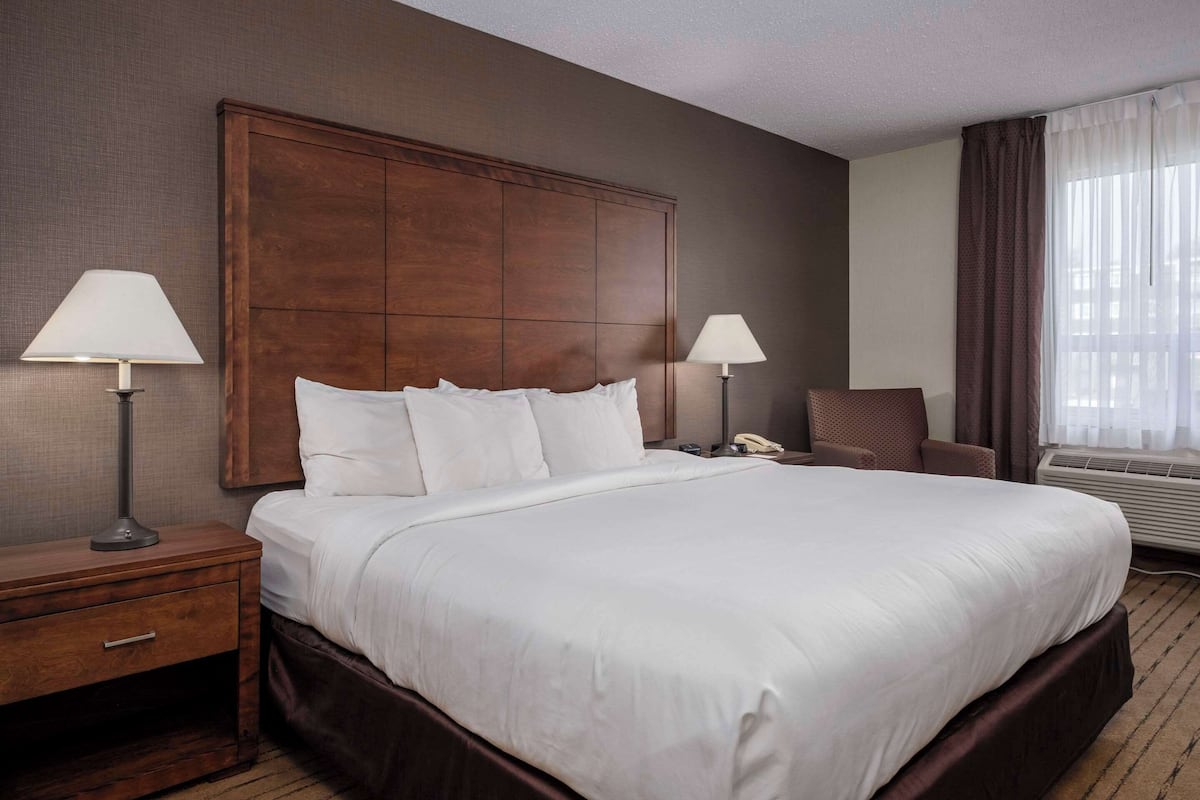A hotel room with a large bed, two bedside lamps, a nightstand, a chair, and a window with curtains.
