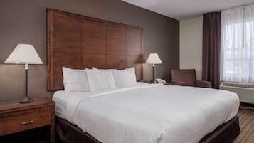 Habitación de hotel con una cama grande, dos lámparas de noche, una mesita de noche, una silla y una ventana con cortinas.