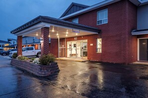 A brick building with a covered entrance, a white van parked in front, and a wet ground.