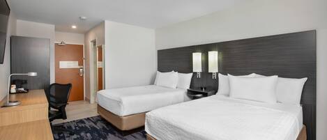 A hotel room with two beds, a desk, a chair, and a TV.
