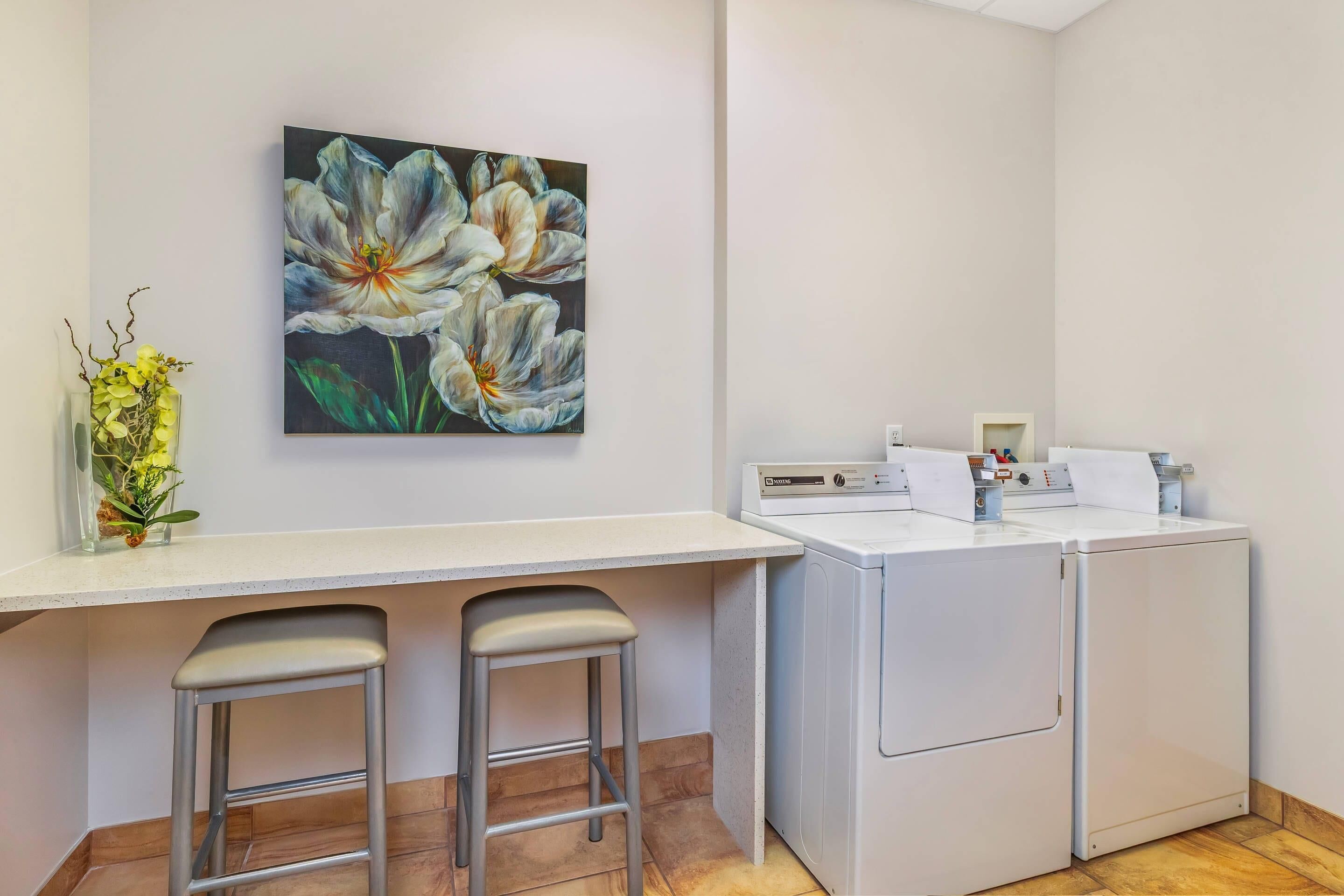 A laundry area with a washing machine, a drying machine, and a painting of flowers on the wall.