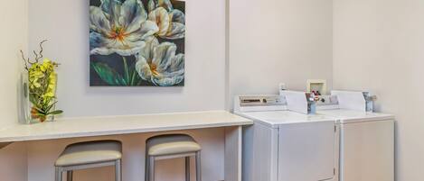 A laundry area with a washing machine, a drying machine, and a painting of flowers on the wall.