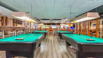 Een poolzaal met meerdere pooltafels, stoelen en een bar.