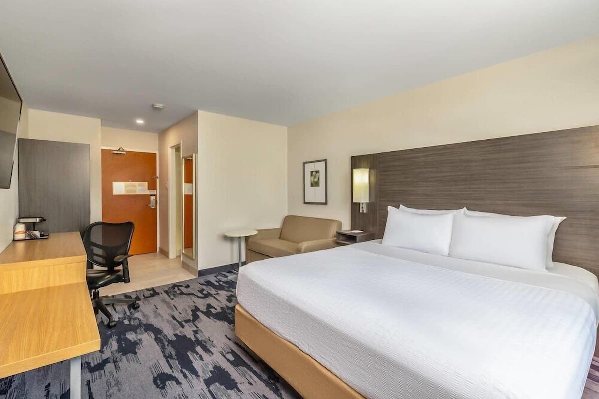 A hotel room with a bed, a desk, a chair, a small table, and a door.