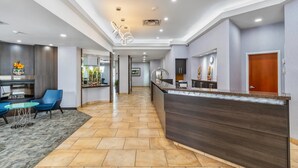 Um hall de hotel moderno com balcão de recepção, área de estar e cozinha visível ao fundo.