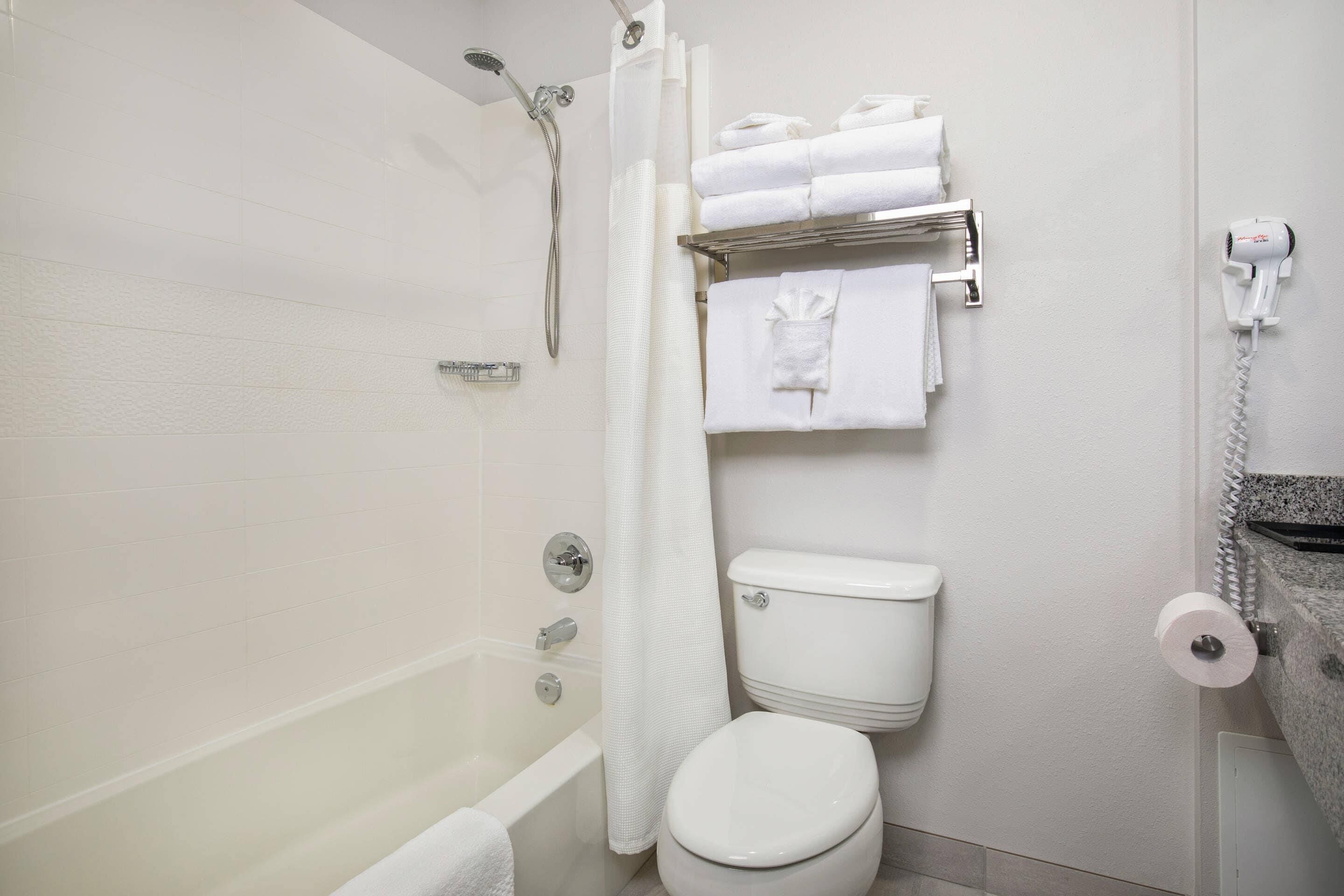 Un baño con bañera, inodoro y toallero con toallas dobladas.