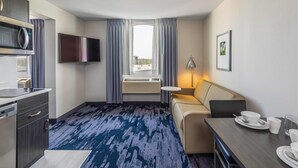 Quarto de hotel com cozinha compacta, televisão de tela plana, sofá, mesa de jantar e janela com cortinas.