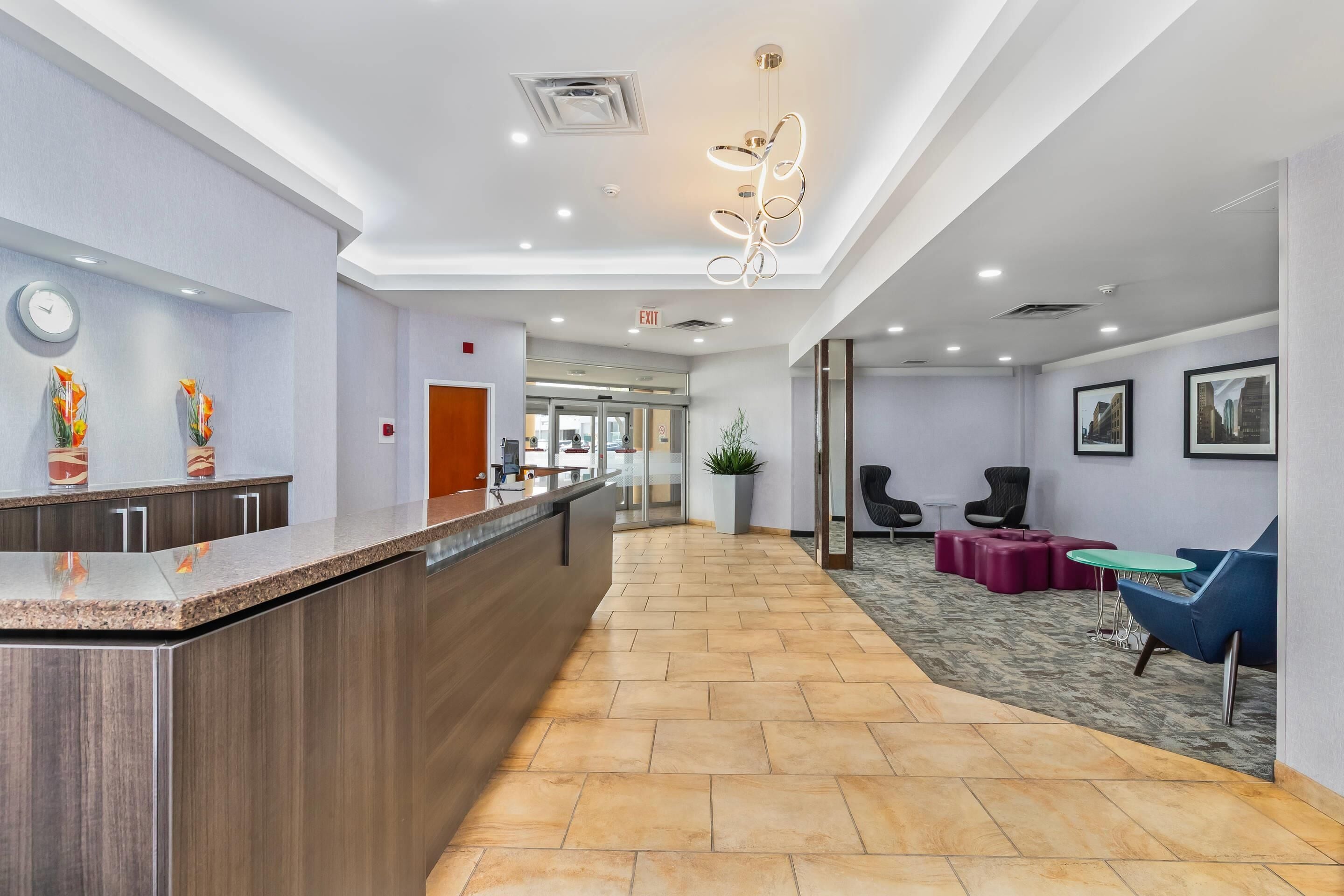 A reception area with a counter, chairs, a plant, and a hallway leading to an exit.
