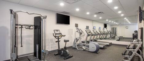 A gym with exercise equipment, a bench, treadmills, and a mirrored wall.