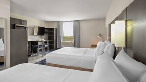 Quarto de hotel com duas camas, uma escrivaninha, uma televisão e uma janela com cortinas.
