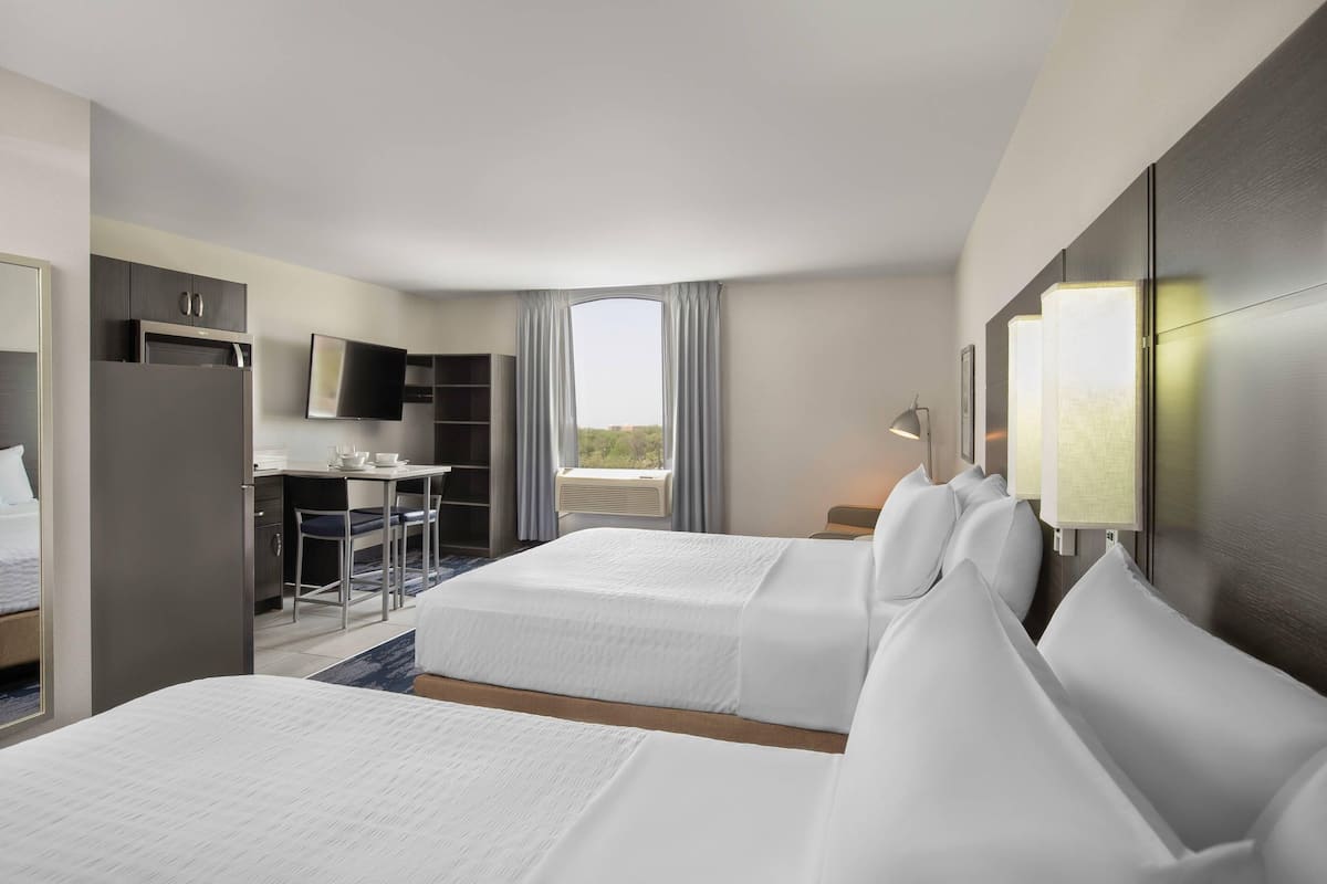 A hotel room with two beds, a desk, a TV, and a window with curtains.
