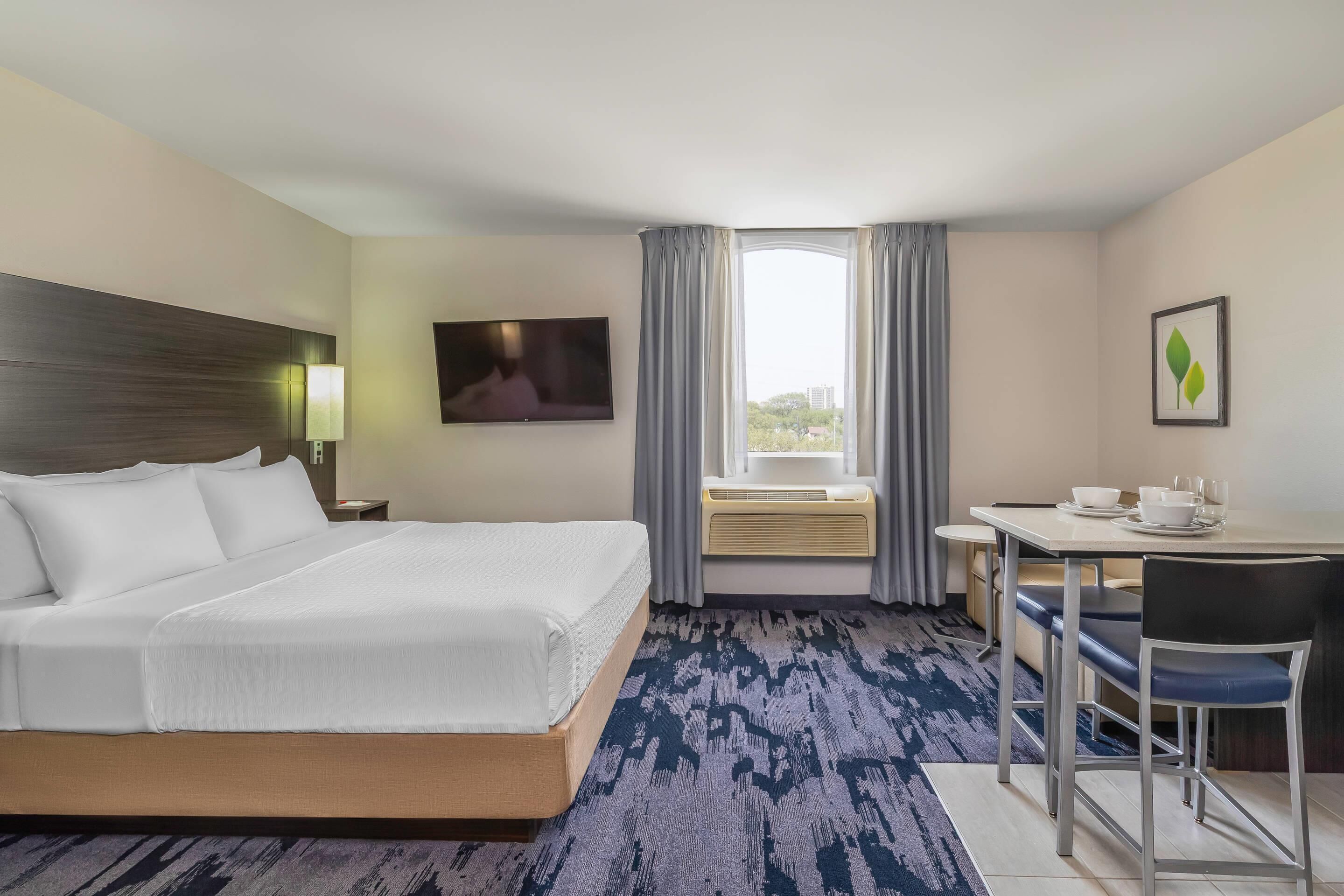 A hotel room with a bed, a desk, a chair, a TV, and a window with curtains.