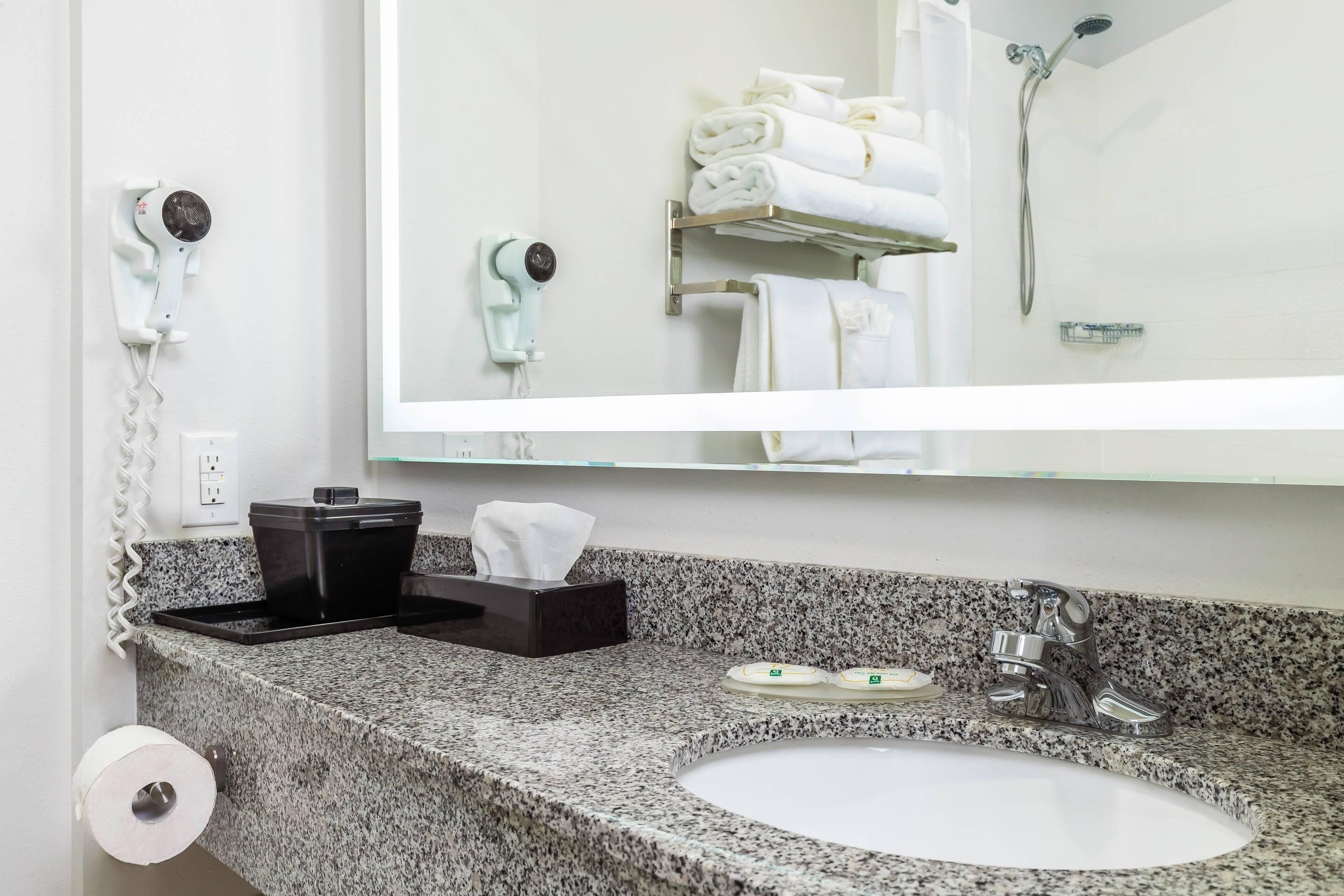 Une salle de bain avec un comptoir en granit, un lavabo, un miroir, un porte-serviettes, un sèche-cheveux et une douche.