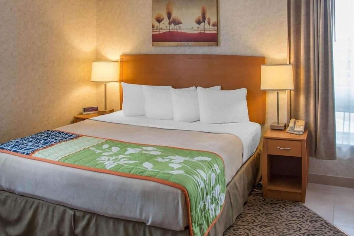 A hotel room with a bed, two bedside lamps, a painting on the wall, and a window with curtains.