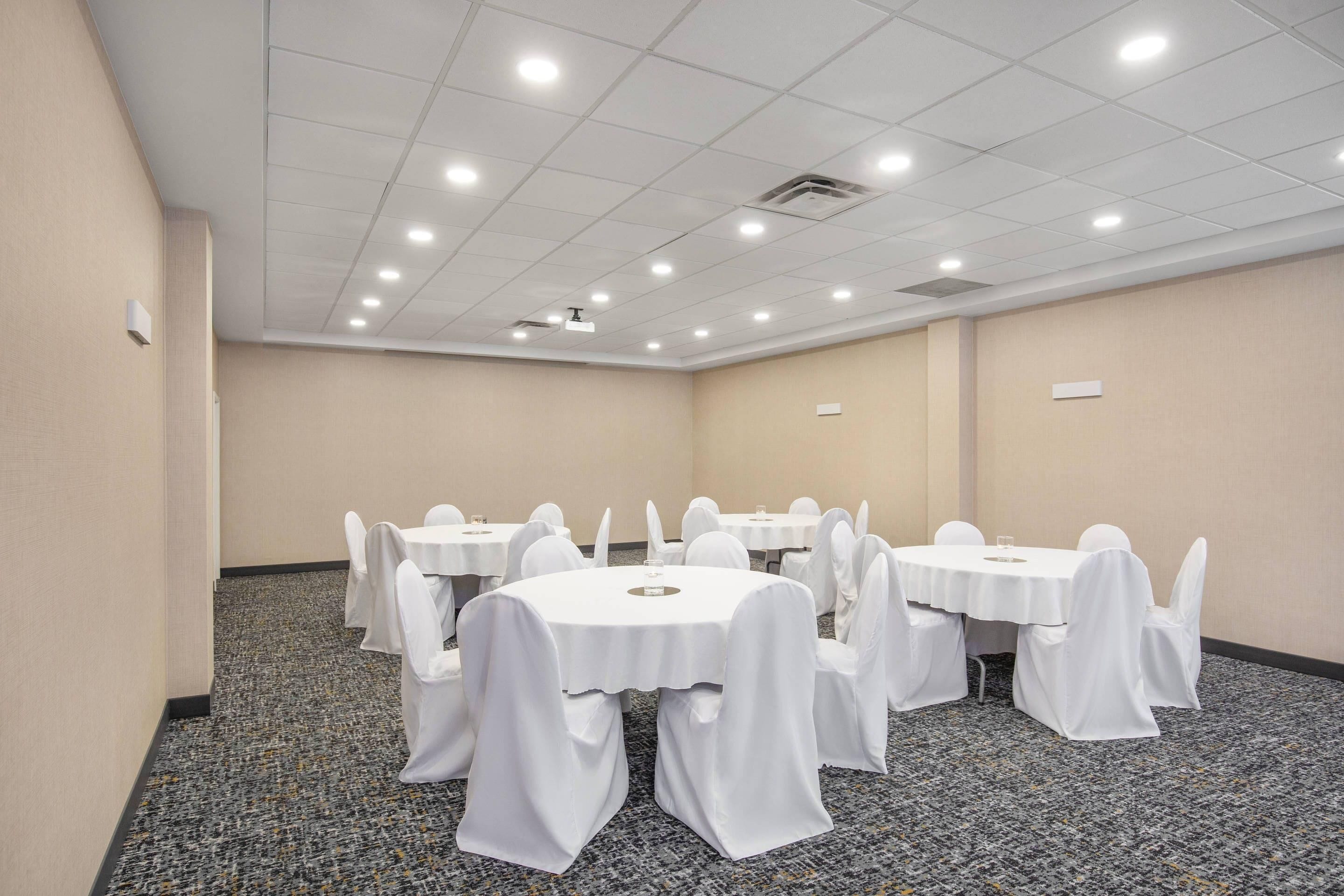 Une salle de conférence avec des tables rondes, des chaises blanches et un revêtement de sol en moquette.
