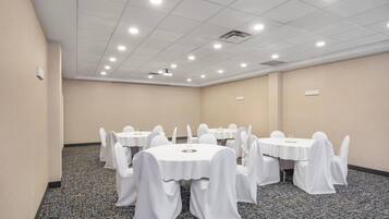Une salle de conférence avec des tables rondes, des chaises blanches et un revêtement de sol en moquette.