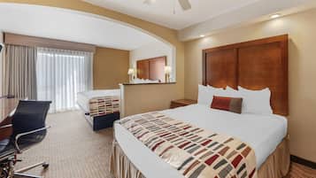 Ein Hotelzimmer mit einem großen Bett, einem Schreibtisch mit Stuhl, einer Schreibtischlampe und einem Deckenventilator.