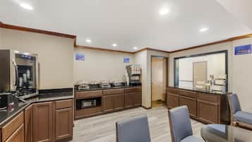 Eine Hotelküche mit Kaffeemaschine, Mikrowelle und Kühlschrank. Im Essbereich stehen Stühle und ein Tisch bereit.