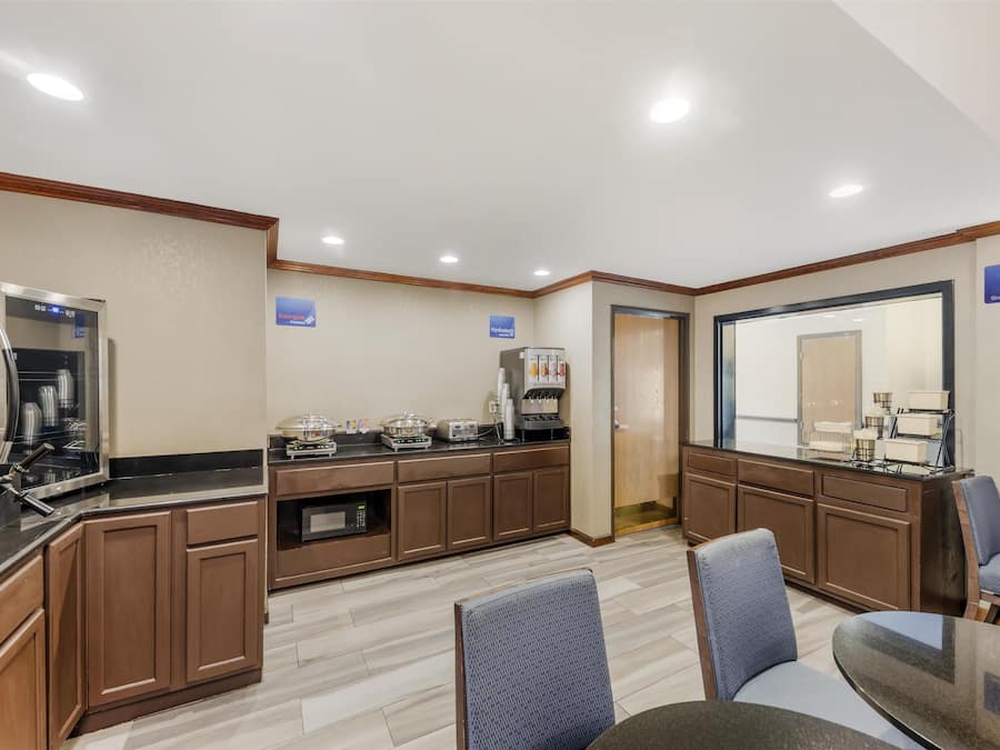 Eine Hotelküche mit Kaffeemaschine, Mikrowelle und Kühlschrank. Im Essbereich stehen Stühle und ein Tisch bereit.