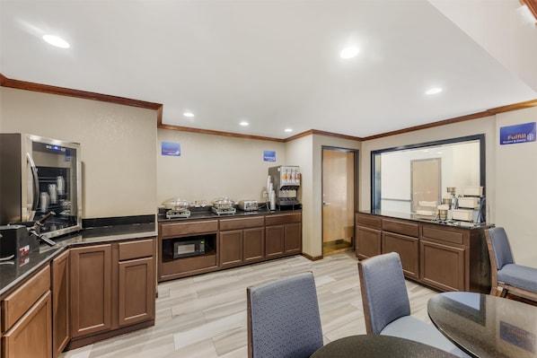A hotel kitchen with a coffee machine, a microwave, and a refrigerator. There are chairs and a table in the dining area. - Best Western Alamo Suites (San Antonio)