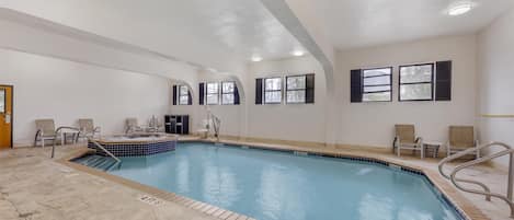 A swimming pool with a hot tub, surrounded by chairs and a changing room.