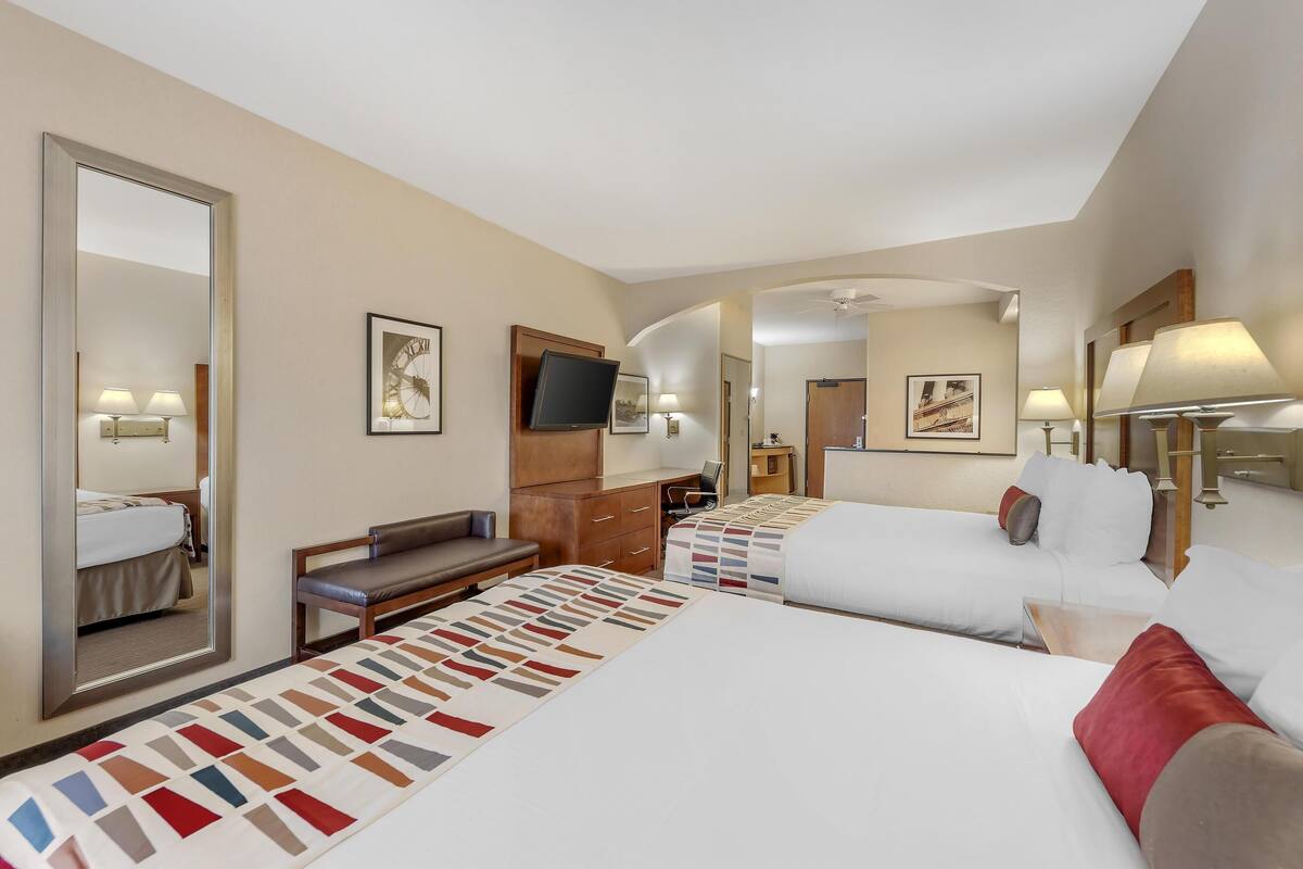 A hotel room with two beds, a desk, a chair, a TV, and a large mirror.