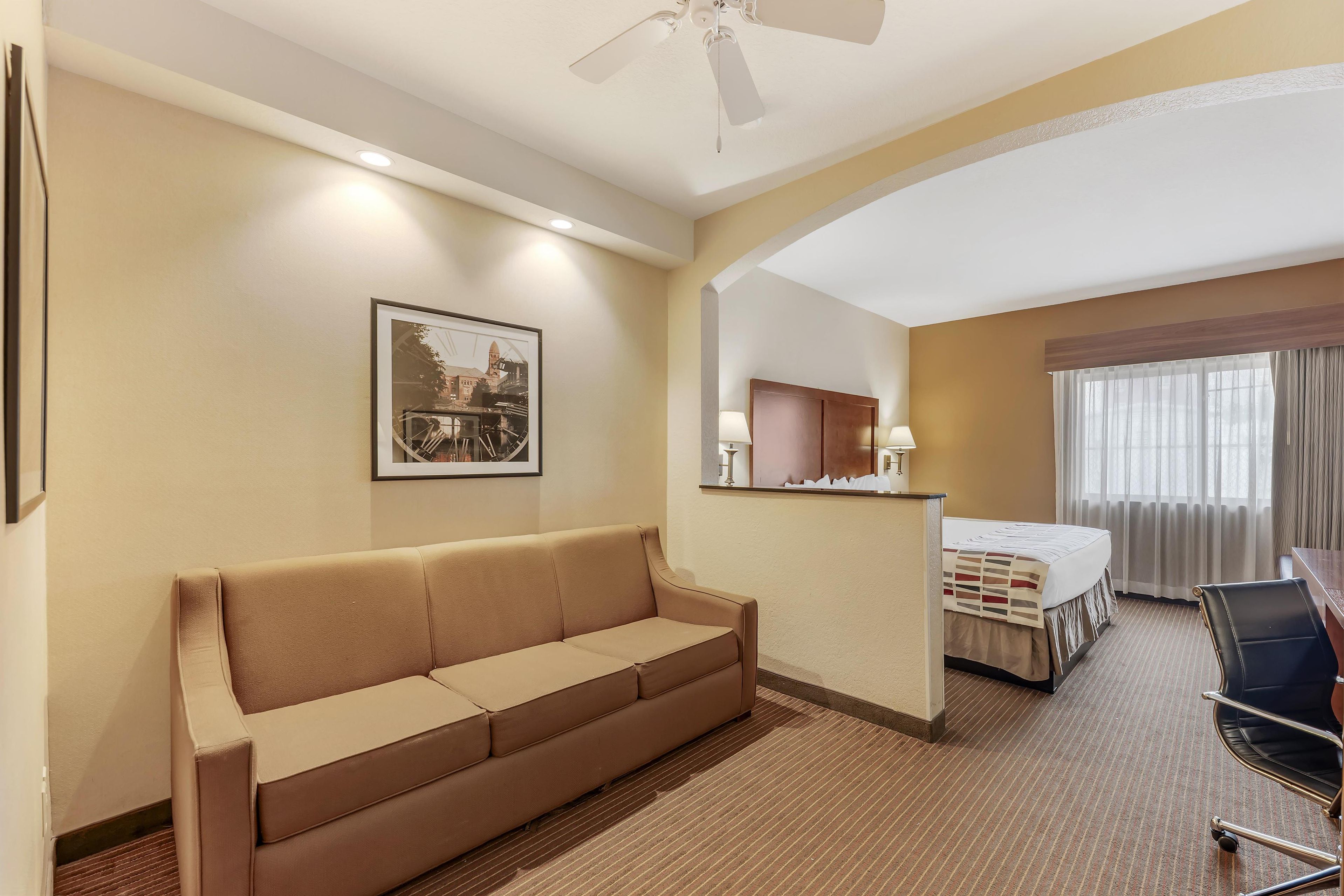 Habitación de hotel con sofá, cama, escritorio y ventilador de techo.