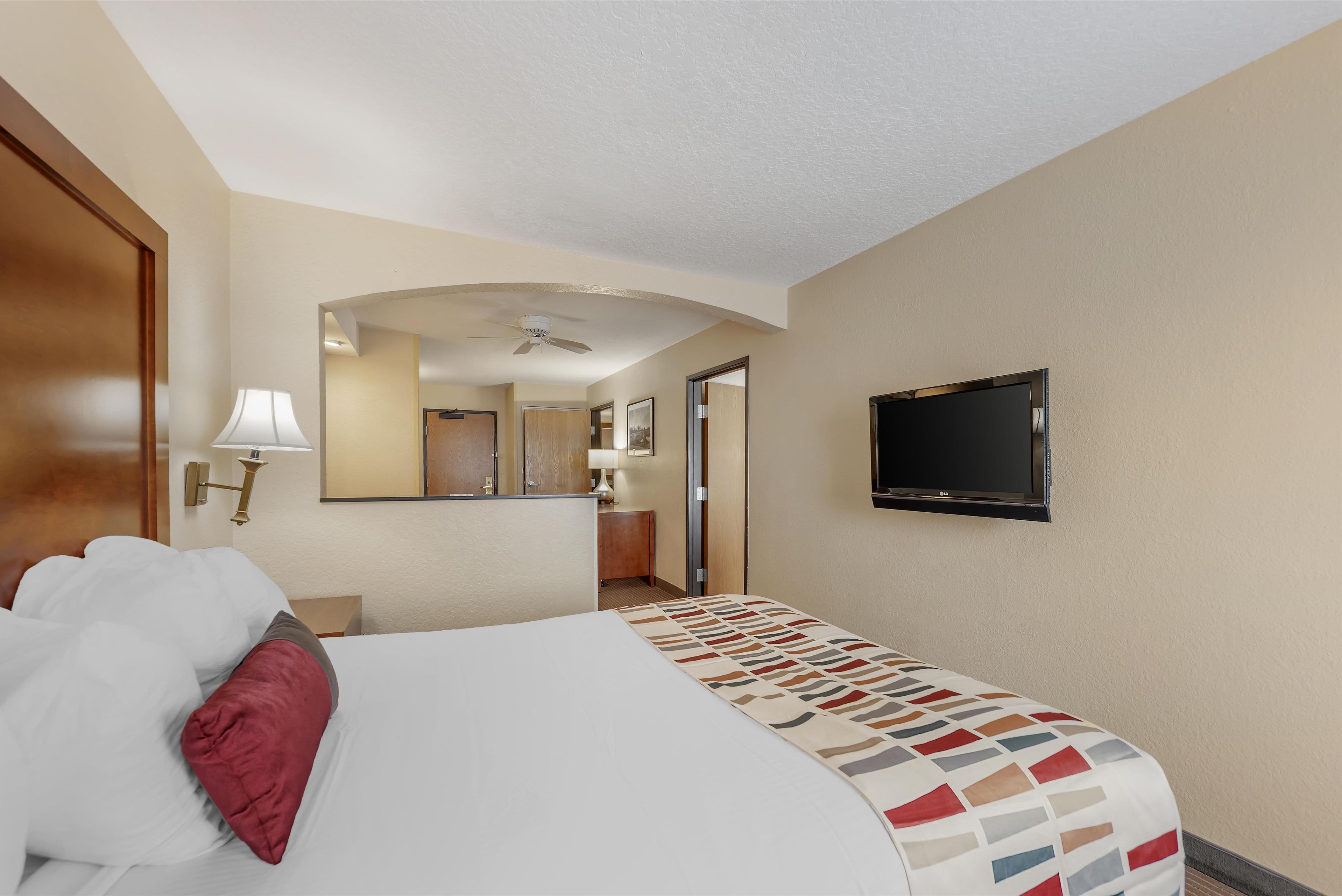 Une chambre d’hôtel avec un lit, un téléviseur fixé au mur, un ventilateur de plafond et un miroir qui reflète la pièce.