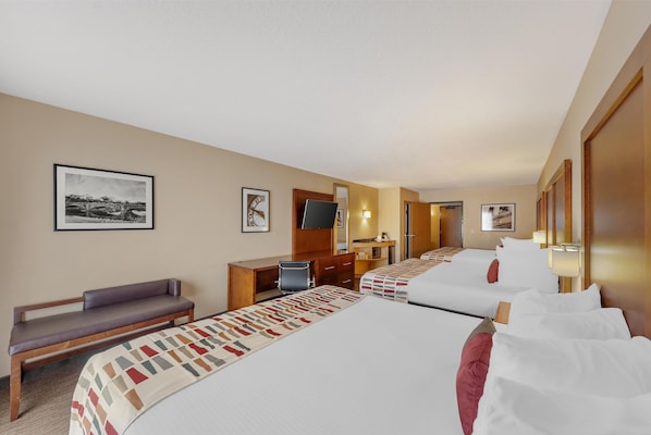 A hotel room with two beds, a desk, a chair, and a bench.