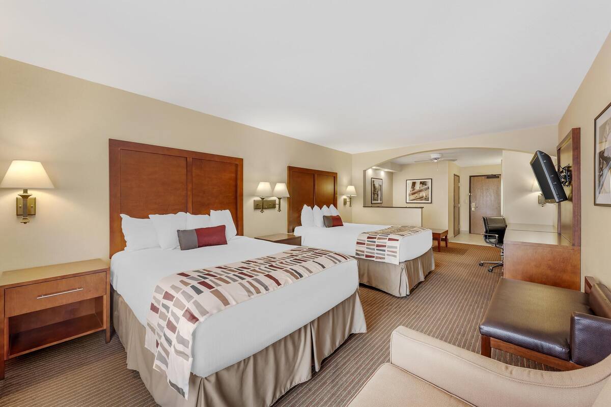 A hotel room with two beds, a desk, a chair, and a bathroom visible in the background.