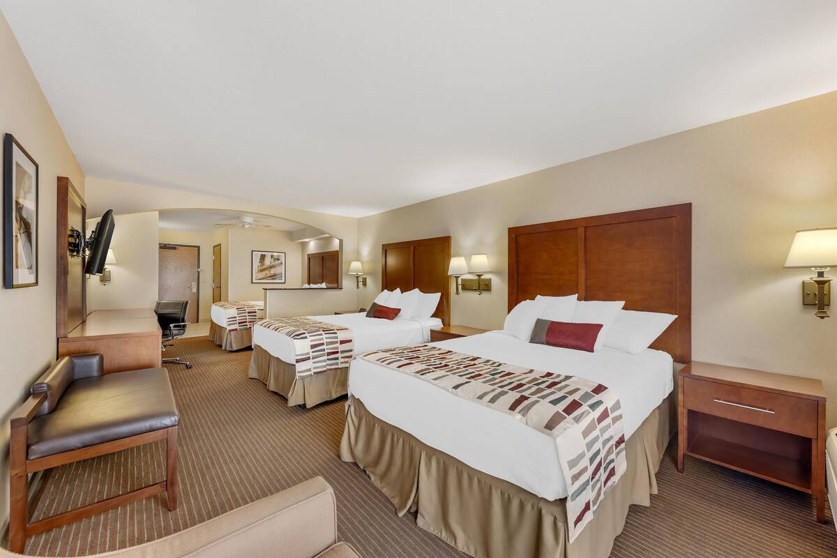 A hotel room with two beds, a desk, a chair, a nightstand, and a lamp.