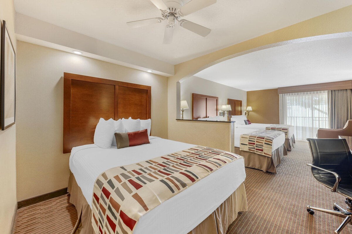 A hotel room with a large bed, a smaller bed, a desk, a chair, and a ceiling fan.