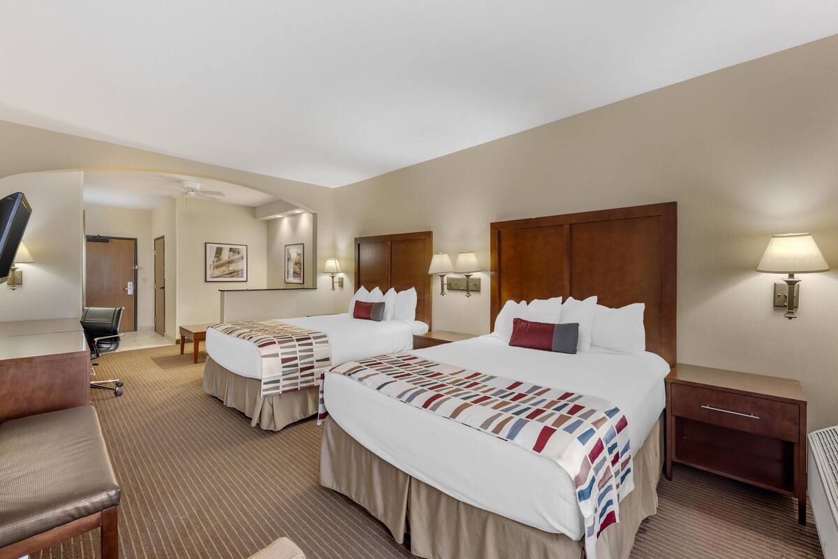 A hotel room with two beds, a desk, a chair, a TV, and a bathroom.