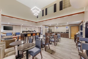 A hotel lobby with multiple seating areas, a kitchen, and a TV screen.