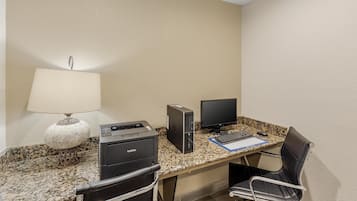 A hotel room with a granite countertop, two monitors, a Brother printer, a black leather chair, and a lamp.