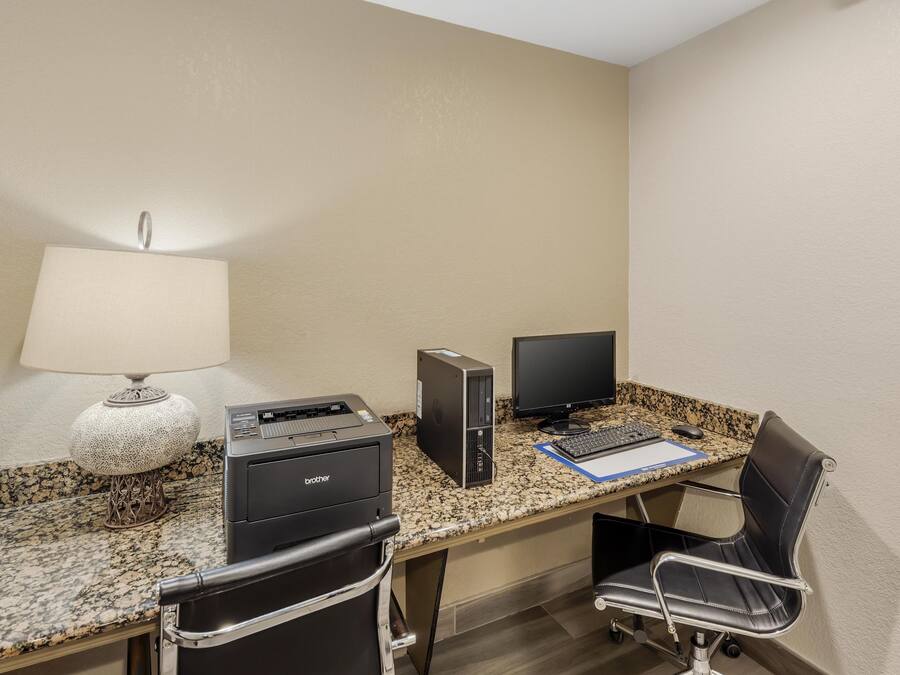 A hotel room with a granite countertop, two monitors, a Brother printer, a black leather chair, and a lamp.