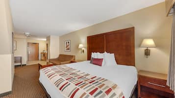 A hotel room with a large bed, a wooden headboard, a bedside table with a lamp, a chair, and a desk with a lamp.