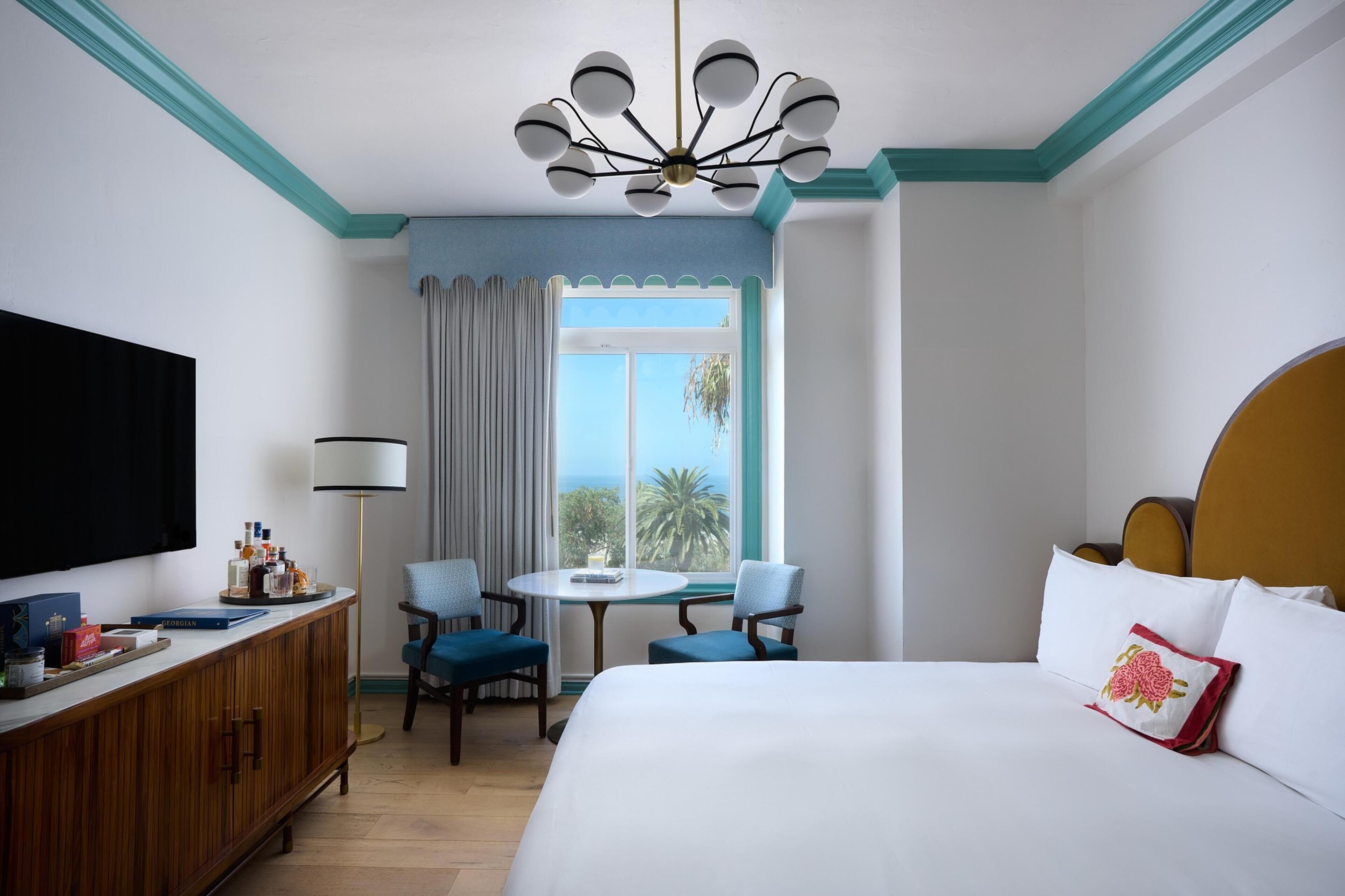 A hotel room with a bed, a desk with chairs, a television, and a window with a view.
