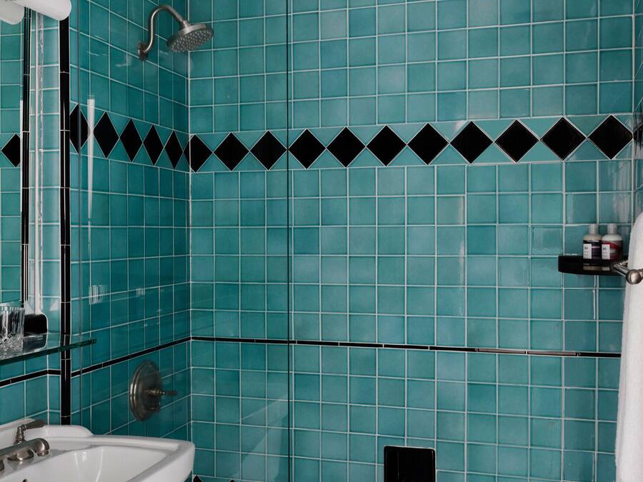 Casa de banho com azulejos verde-água, uma moldura em padrão de losangos preto e branco, uma pia branca e área de duche.