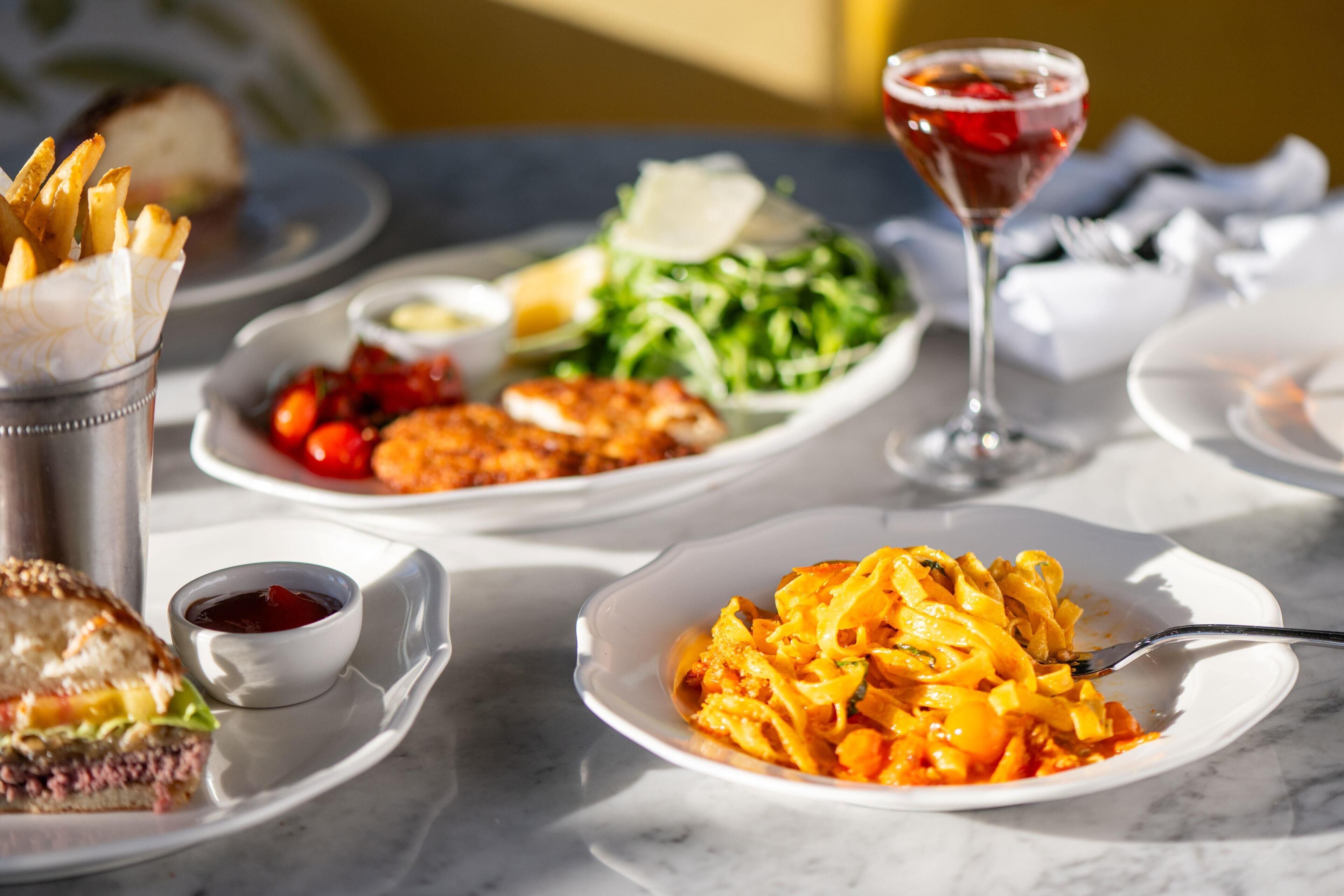 Una mesa con varios platos, entre ellos pasta, papas fritas, ensalada y un martini.