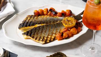 A dining table with a plate of grilled fish, artichokes, and a glass of red wine.