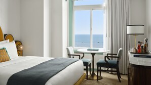 A hotel room with a bed, two chairs, a small table, a lamp, and a view of the sea. - The Georgian, in The Unbound Collection by Hyatt (Santa Monica)