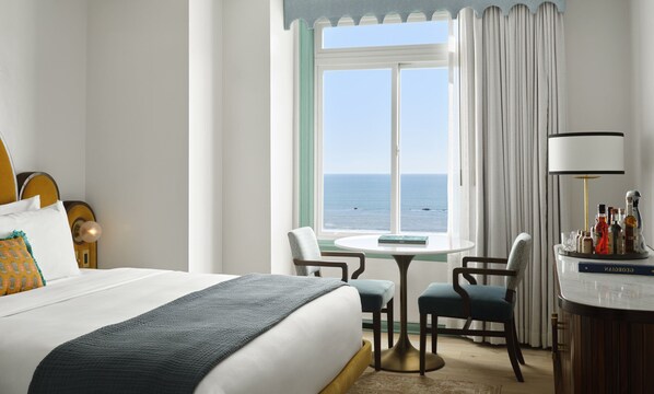 A hotel room with a bed, two chairs, a small table, a lamp, and a view of the sea. - The Georgian, in The Unbound Collection by Hyatt (Santa Monica)