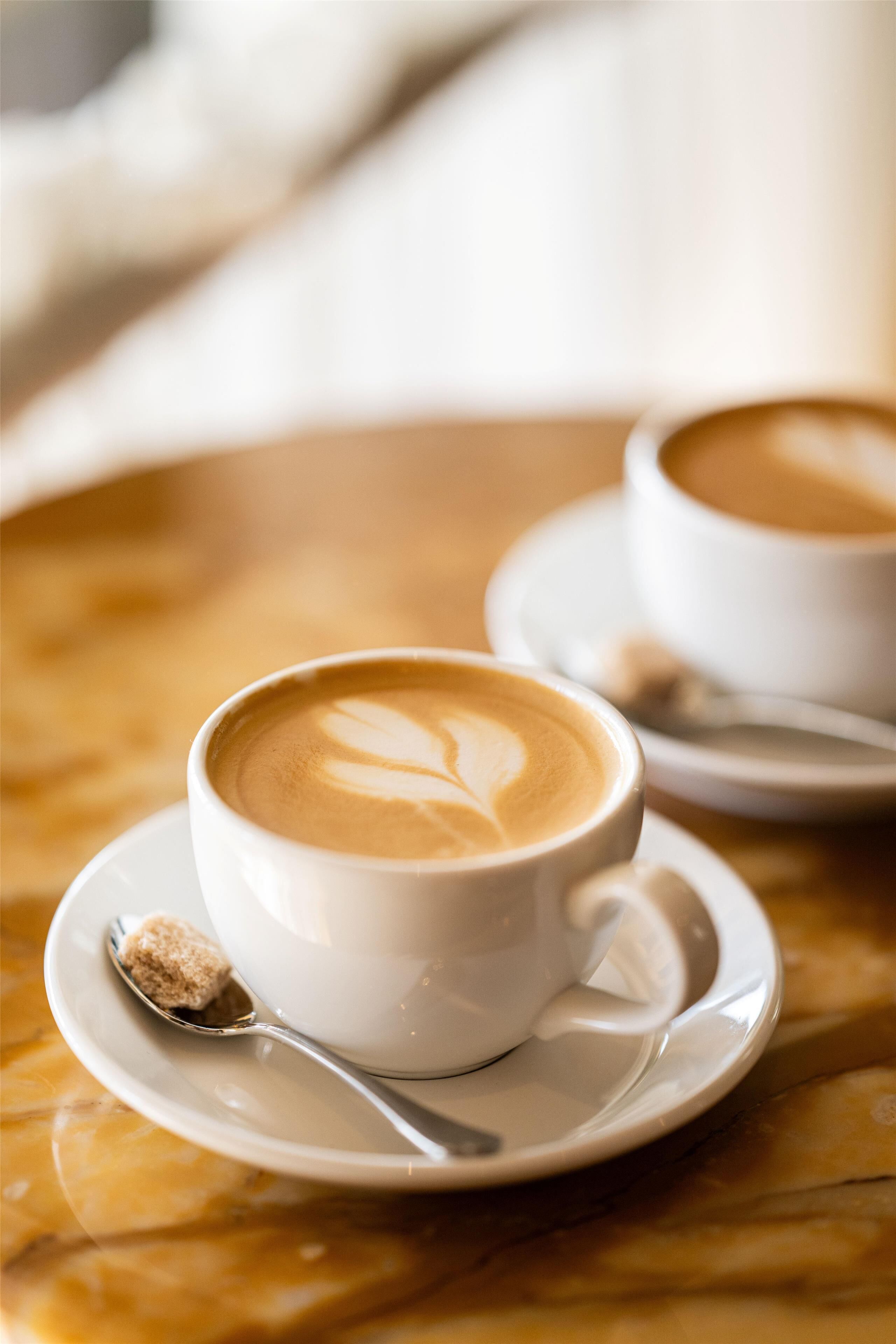 Une tasse de café ornée d’un motif en latte, posée sur une soucoupe, le tout sur une table en marbre.