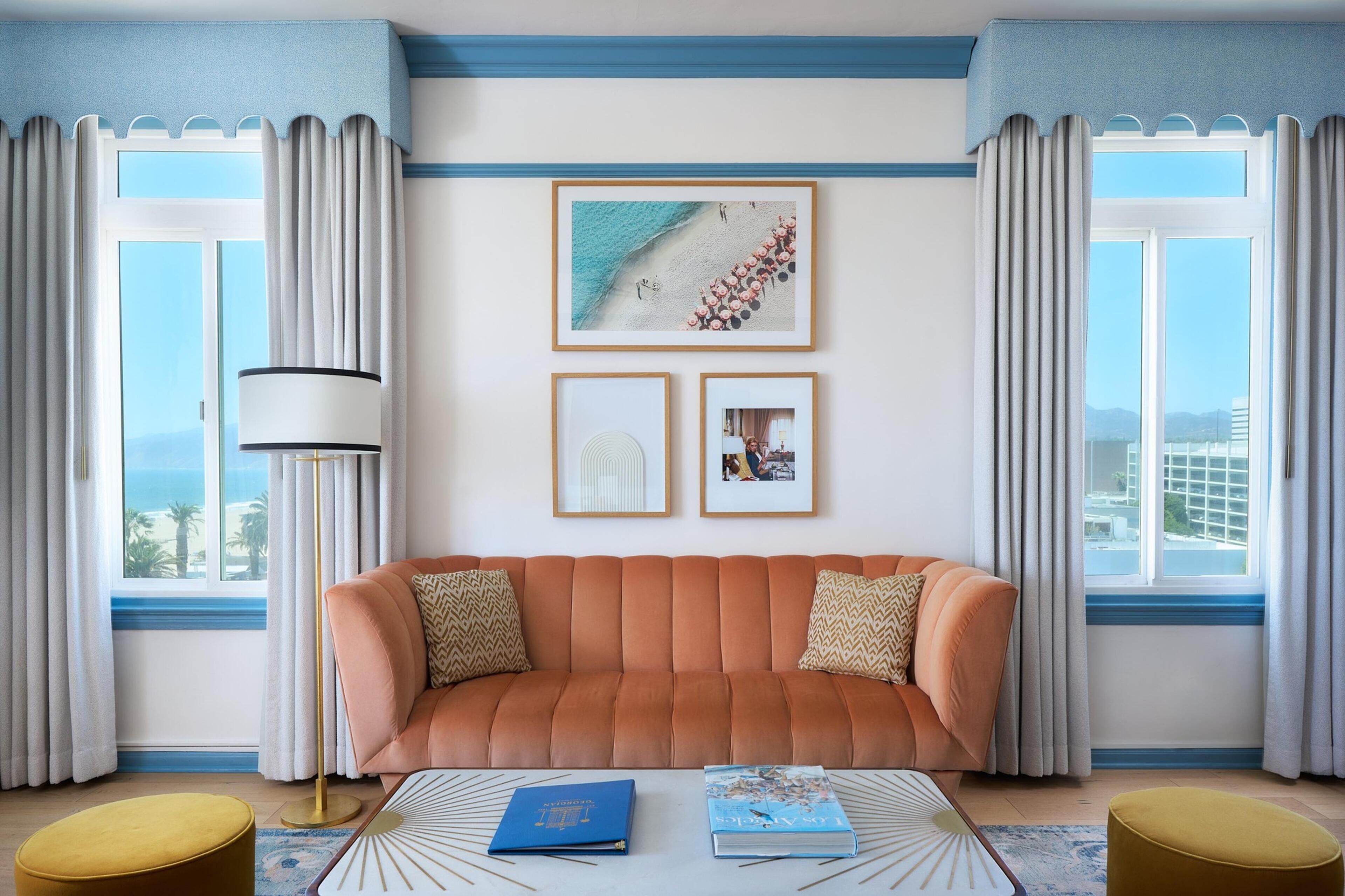 A living room with a sofa, two framed pictures, a floor lamp, and a view of the beach through large windows.