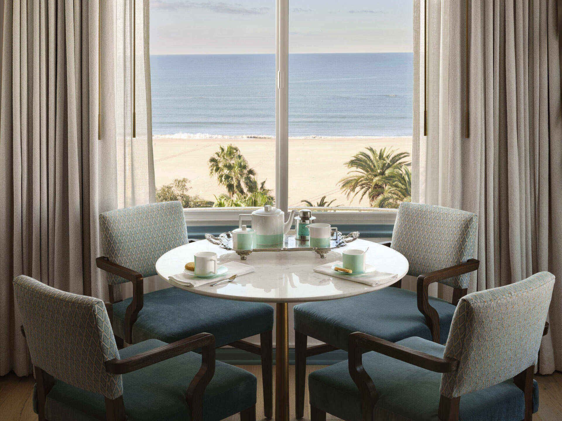 A dining area with a table set for four, overlooking a beach with palm trees.