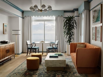 A hotel room with a bed, a round table, two chairs, a desk with a lamp, and a view of the sea. at The Georgian, in The Unbound Collection by Hyatt