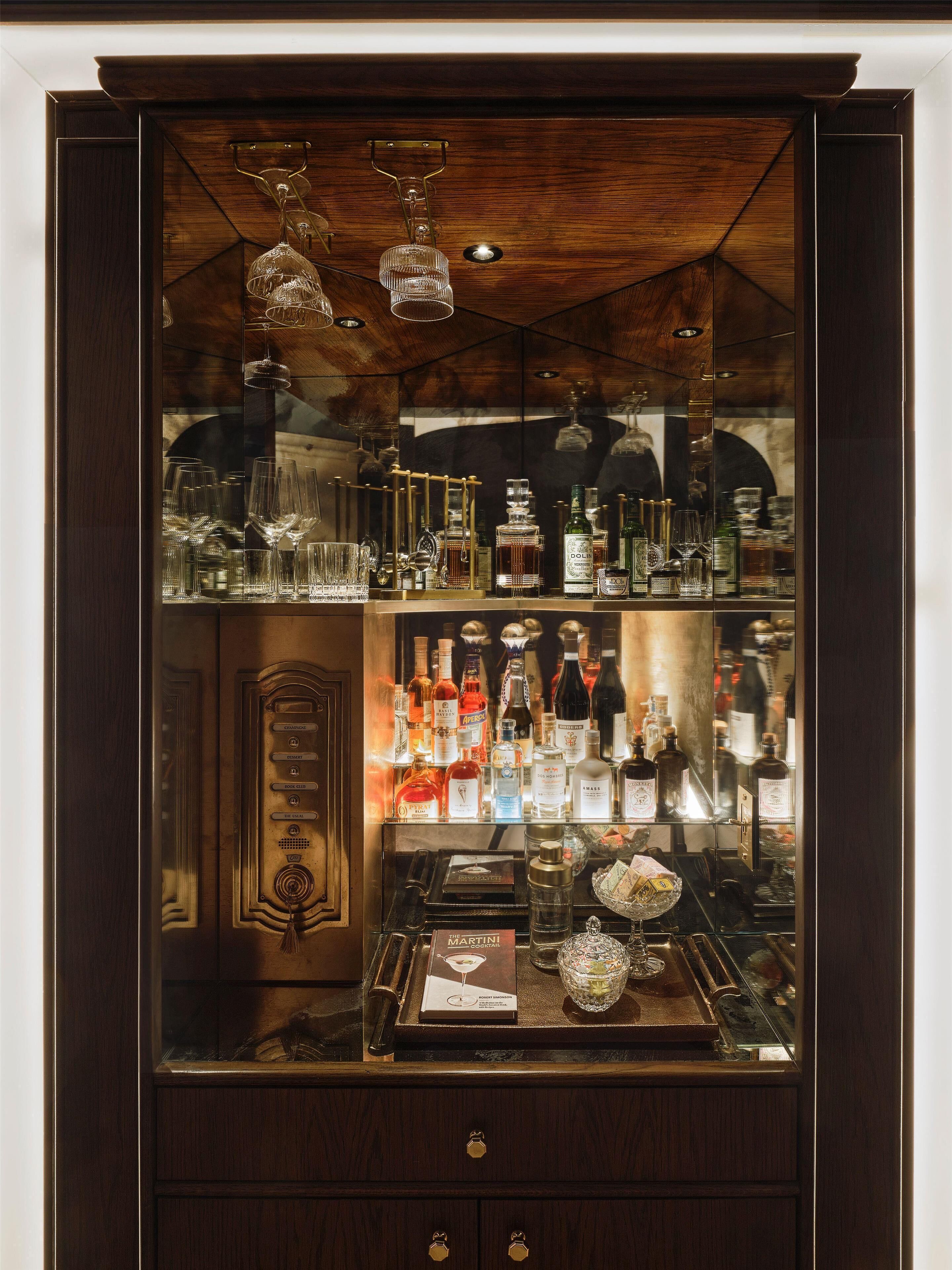 Eine Barbereich mit einem Holzkabinett, Regalen mit Spirituosenflaschen, Gläsern und einem Martini-Glas auf der Theke.